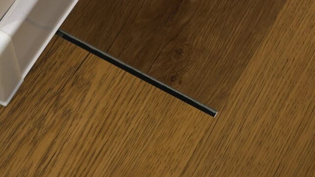 Damaged vinyl flooring with a separated locking system gap near the baseboard. Renovation, repair, floor installation, and maintenance concept