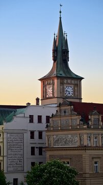 Vertical view of a clock tower with a green spire above a sgraffito-decorated facade, Prague, Czech Republic