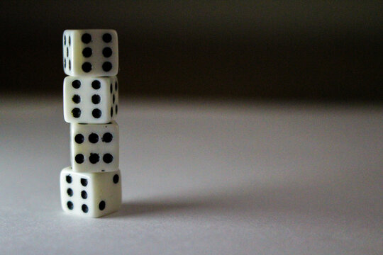 Four stacked white dice with black dots cast shadows on a white surface