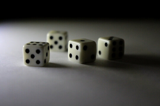Four white dice with black dots cast shadows on a white surface