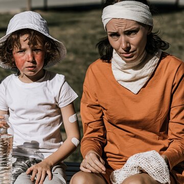 Young child with heat exhaustion and flushed cheeks sitting with a caregiver in the shade on a park bench for summer safety and health awareness