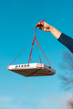 box of pizza in the hand is suspended on a ribbon