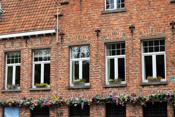Naklejka premium Brick building facade with multiple windows adorned with flower boxes and colorful floral decorations, showcasing traditional architecture in a charming urban setting