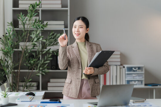 A Visionary businesswoman at her desk, poised to share an innovative idea with a focused gaze and a gentle smile, surrounded by office essentials and lush greenery.