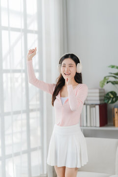 Happy Girl Listening Music: A cheerful young woman with headphones on dances joyfully in a sunlit room, lost in the rhythm of her favorite song.