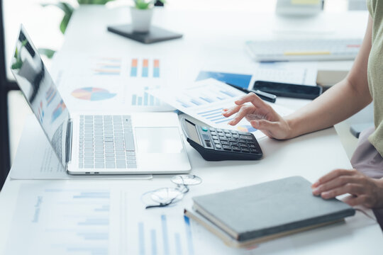 Analyzing Financial Data: A person's hands are shown calculating numbers on a calculator with a laptop and financial charts on a desk, emphasizing financial analysis and accounting tasks.