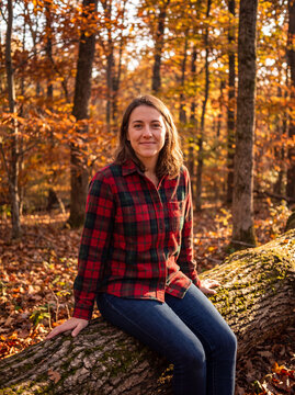 Smiling woman sitting on fallen log in sunlit autumn forest