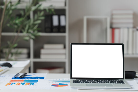 A close-up shot of a digital tablet with a blank white screen on an office desk, surrounded by business charts and graphs