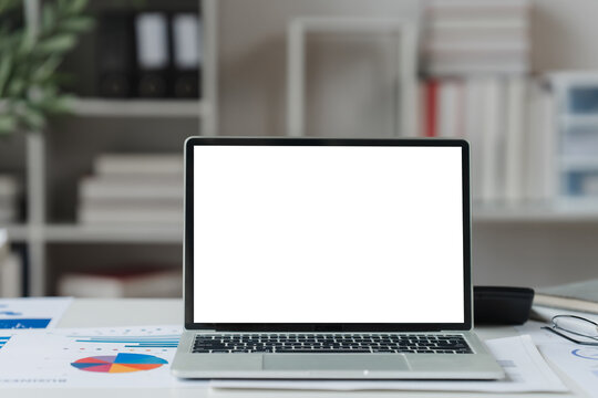 A close-up shot of a digital tablet with a blank white screen on an office desk, surrounded by business charts and graphs