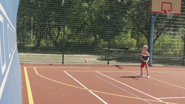 Slow motion. 7-year-old boy training his tennis skills against a practice wall