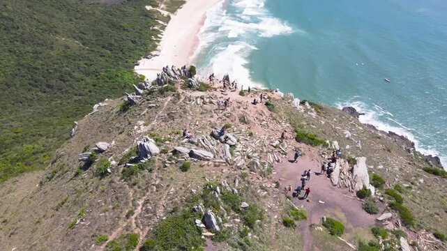 Drone Orbit Lift View of Hikers on Morro da Coroa Mountain Ridge in Florianopolis Brazil, Summit Revealing Lagoinha do Leste Beach Sand and Ocean Waves, Adventure Travel Footage

