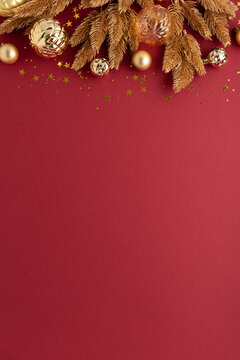 Festive golden Christmas ornaments and pine branches scattered with glitter on a rich red background