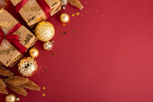 Christmas presents and golden baubles arranged on a deep red background with sparkling confetti creating a festive holiday scene