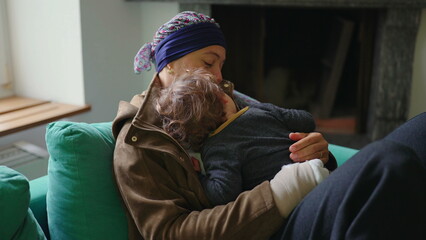 Fototapeta premium Mother recovering from cancer embracing toddler on sofa at home, family support moment highlighting healing, resilience, attachment and emotional strength