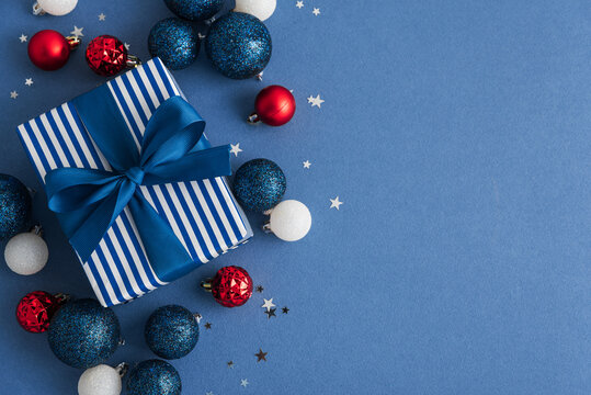 Festive Gift Box Surrounded by Christmas Ornaments and Star Confetti on Blue Background