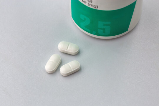 White pills and medicine bottle with 2.5 mg label, closeup.