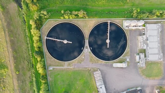 Circular sedimentation tanks with rotating clarifier arms at a modern wastewater treatment plant on summer day cleaning water, top down aerial