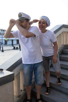 Middle aged couple in captain and sailor hats looking away on river station embankment