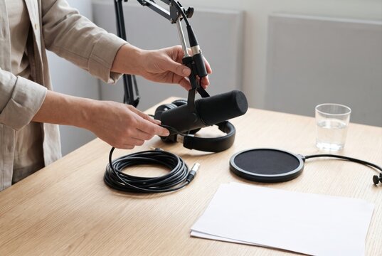 Hands adjusting a black studio microphone on a desk boom arm next to headphones