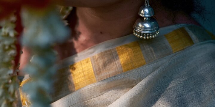 Traditional silver jhumka earring and gold border of a kasavu saree worn by a woman, featuring soft morning light and an elegant heritage mood for ethnic fashion and cultural themes