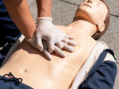 A close-up view of hands in medical gloves performing chest compressions on a CPR training mannequin.