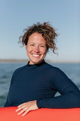 Fototapeta premium Happy woman in wetsuit holding red surfboard by the sea for outdoor sports portrait and active lifestyle banner
