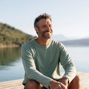 Mature man sitting on a wooden dock by a peaceful lake for contemplative portrait background and wellness lifestyle design