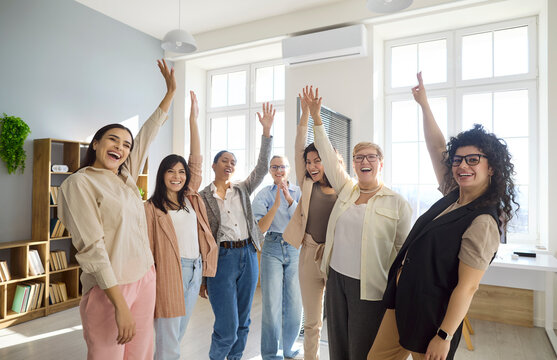 Women team celebration shows success and victory. Colleagues raise hands in bright office, cheering results and milestones. Great for leadership and branding. Concept of victory, unity and joy.
