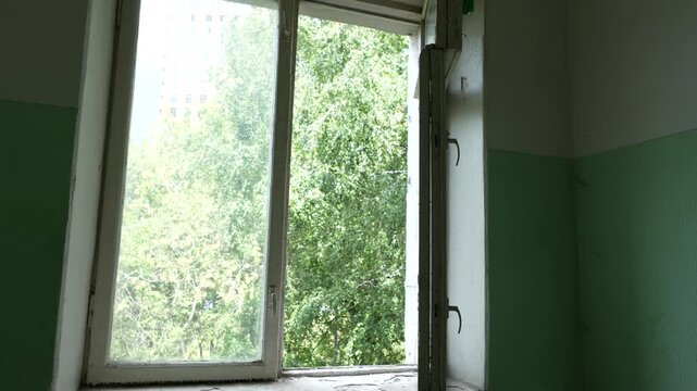 Interior of an old residential building entrance with open window showing worn walls, natural light and the need for renovation and maintenance work