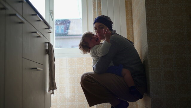 Mother comforting upset toddler with affectionate embrace on kitchen floor, nurturing parent child interaction expressing attachment, emotional security, reassurance and loving support