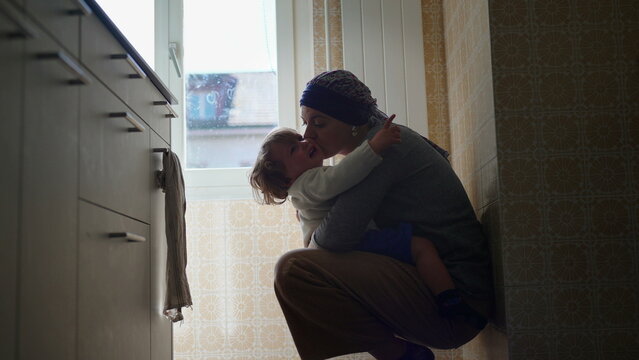 Mother comforting upset toddler with affectionate embrace on kitchen floor, nurturing parent child interaction expressing attachment, emotional security, reassurance and loving support