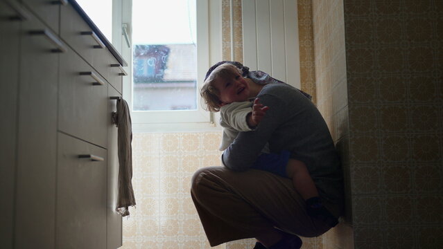 Mother comforting upset toddler with affectionate embrace on kitchen floor, nurturing parent child interaction expressing attachment, emotional security, reassurance and loving support