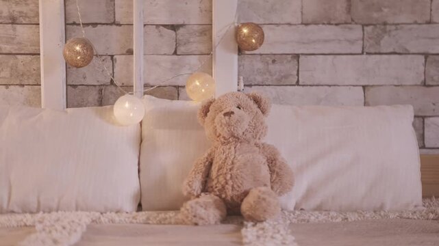 Bed with unlit decorative fairy lights in bedroom, teddy bear resting, soft beige blanket with white pillows, glowing string fairy lights in background, cozy calm home atmosphere, Evening relaxation