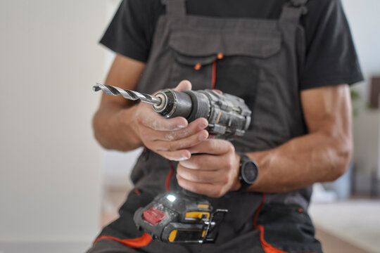 Worker holding a cordless drill with drill bit indoors. Concept of home renovation