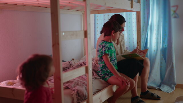 Mother helping son develop reading skills before bedtime while toddler explores nearby creating authentic family learning environment focused on education parenting