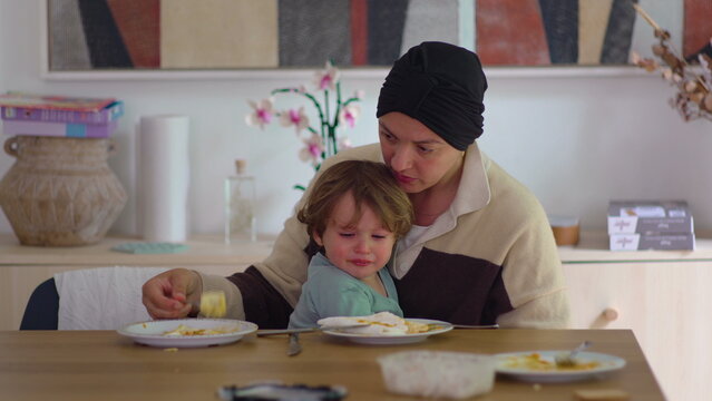 Mother comforting crying toddler at dining table in family home during cancer recovery, highlighting maternal care, emotional support, attachment, resilience and family connection