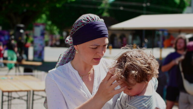 Mother holding toddler child during outdoor community gathering, affectionate parent child moment highlighting attachment, security, care and family connection