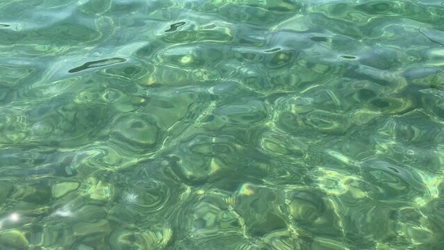 Crystal clear tropical water surface seen close up near shore, sunlight dappling through gentle ripples creating vibrant natural patterns ideal for summer vibes