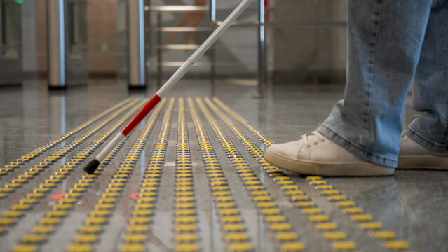 A blind woman walks on tactile paving. Close-up of her feet and a walking stick.