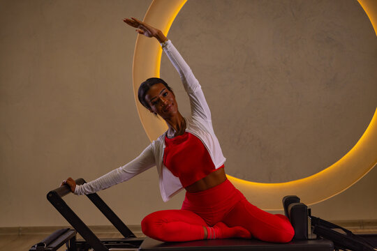 Woman exercising on a Pilates Reformer in a modern wellness studio, with a glowing crescent moon design in the background. Fitness, strength, flexibility, and mindful movement.