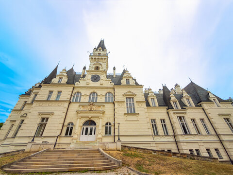 Front entrance facade of Budmerice Manor with stone stairs. Wide angle view of historic yellow palace building with central staircase and clock tower.