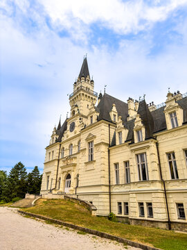 Historic Budmerice Manor castle facade under cloudy blue sky. Low angle exterior view of yellow palace building with clock tower in Slovakia.