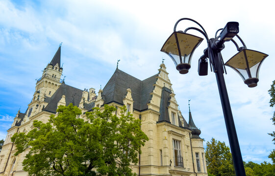 Black street lantern post with security camera near historic castle. Close view of metal lamp pole with video surveillance device in front of yellow building.
