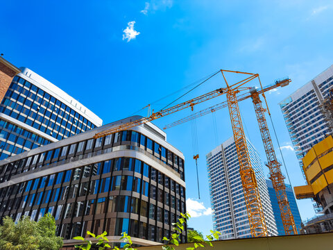 Construction site with cranes in a city. Workers are building tall buildings in the city with cranes and scaffolding under a blue sky.