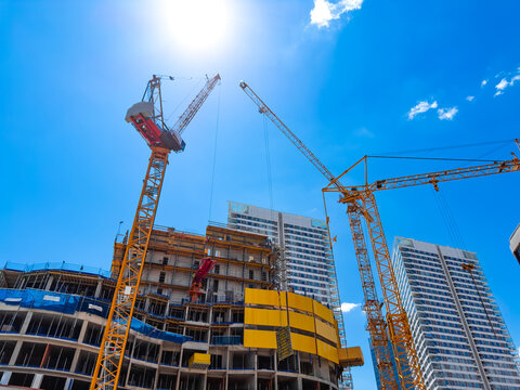 Construction under clear skies. Workers use cranes to lift materials at a building site in an urban area during bright daylight.