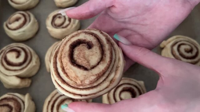 Baker carefully tucking the end of an unbaked cinnamon roll before placing it on a baking sheet