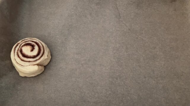 Female hands carefully placing raw cinnamon rolls onto a baking sheet with parchment paper