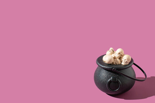 Black witch cauldron loaded with skulls on a purple background. Funny Halloween holiday concept.
