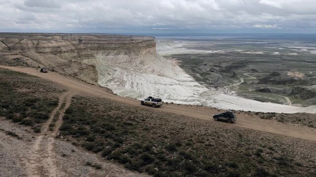 Aerial view of off-road vehicles driving on a dirt track along the white limestone cliffs of Bozjyra in Aktau, Mangystau Region, Kazakhstan.