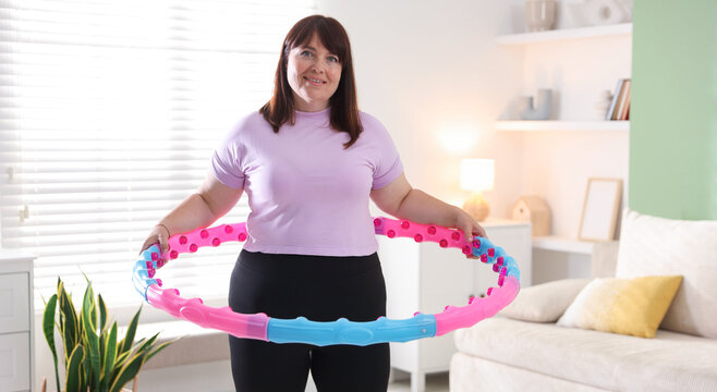 Overweight woman exercising with hula hoop indoors. Sports equipment